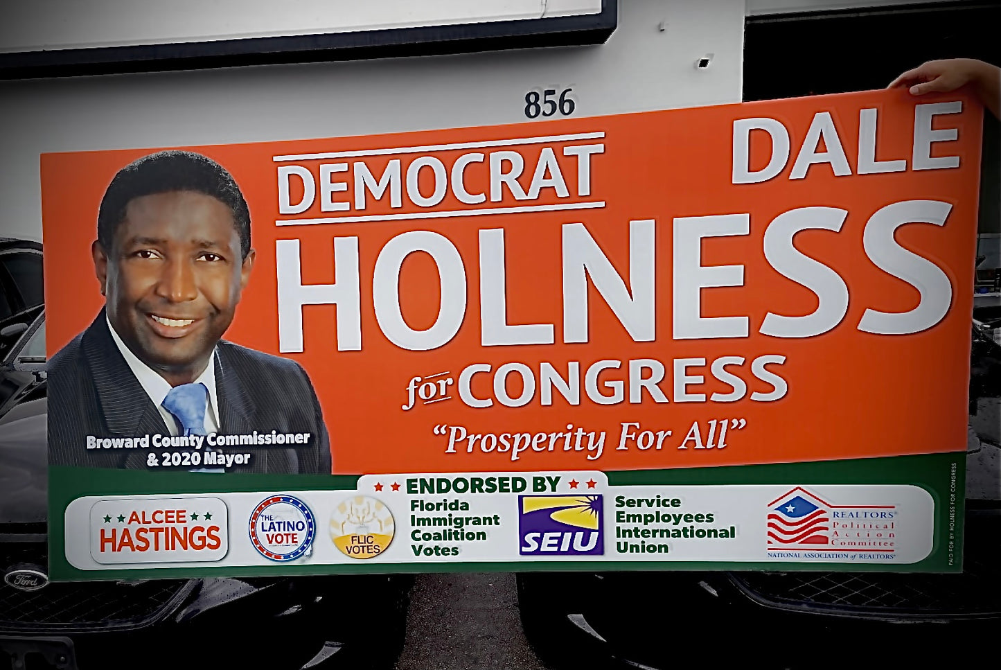 Political campaign sign for Dale Holness for Congress with a photo of the candidate on an orange background.
