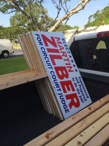 Stack of political campaign signs for Martin Zilber on a wooden surface with a vehicle in the background.