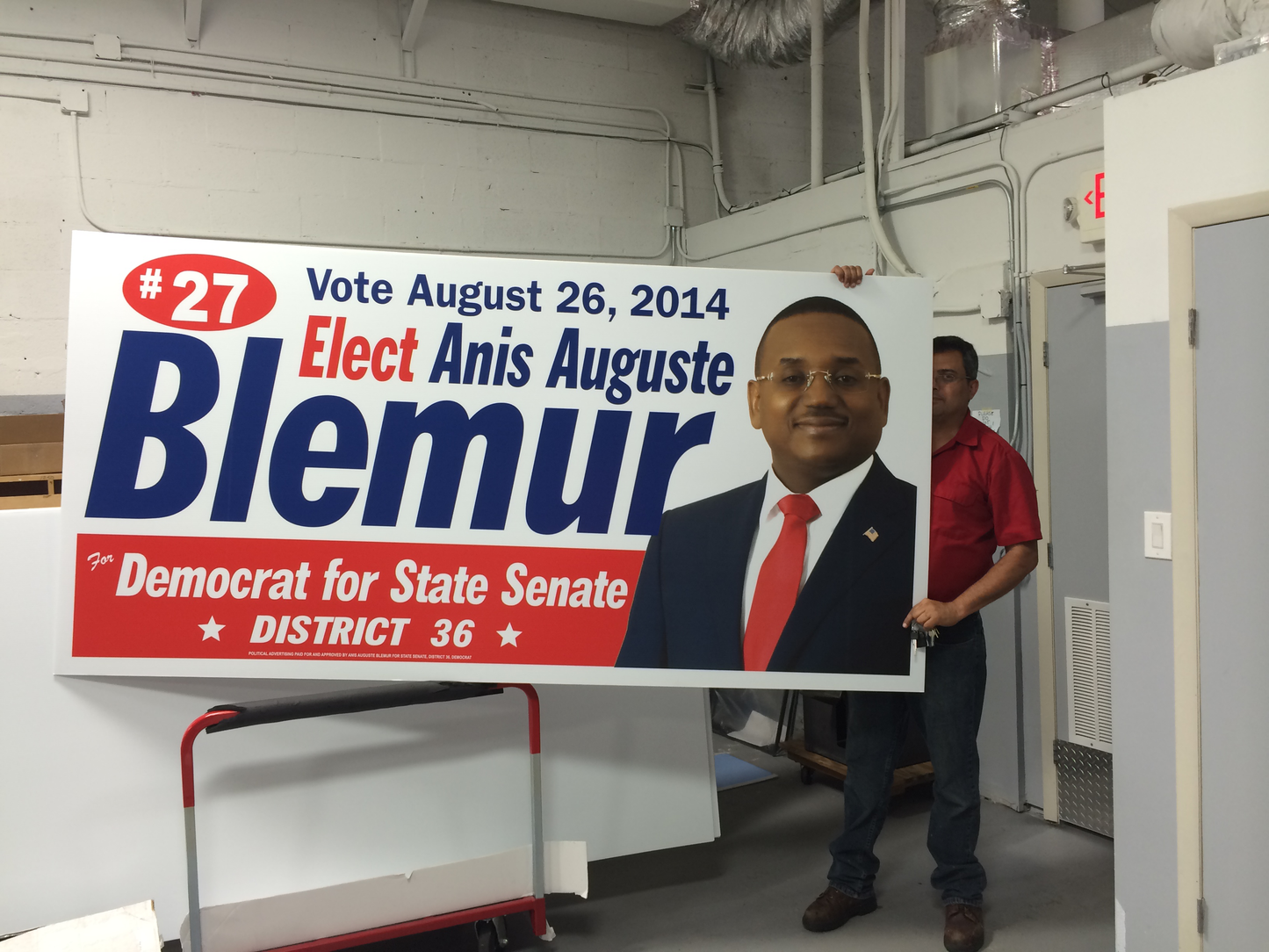 Person holding a political campaign sign for Anis Auguste Blemur in an indoor setting.