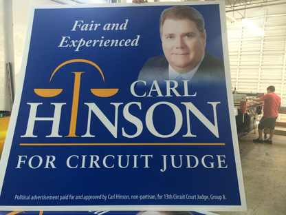 Political campaign sign for Carl Hinson for Circuit Judge in a warehouse setting.